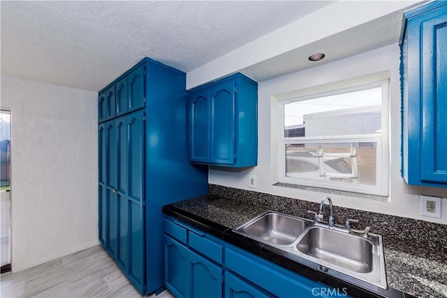 kitchen featuring dark countertops, blue cabinetry, a textured ceiling, and a sink