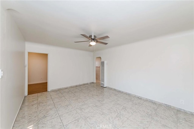 unfurnished room featuring arched walkways, ceiling fan, and baseboards