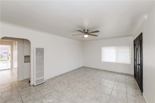 spare room with a heating unit, arched walkways, baseboards, ceiling fan, and light tile patterned flooring