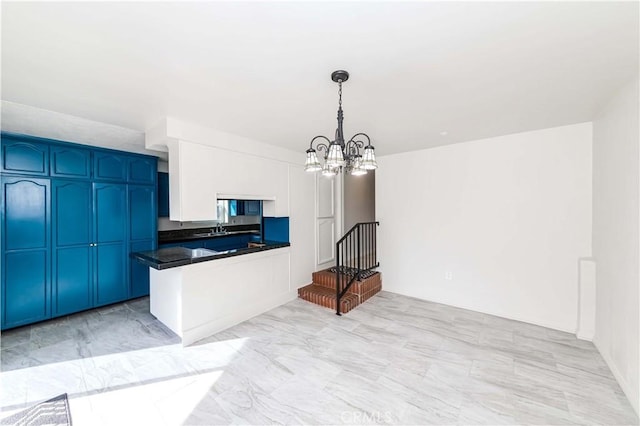 kitchen with dark countertops, decorative light fixtures, a peninsula, an inviting chandelier, and a sink