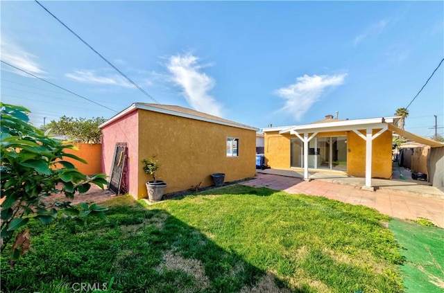 rear view of property featuring a patio, fence, a lawn, and stucco siding