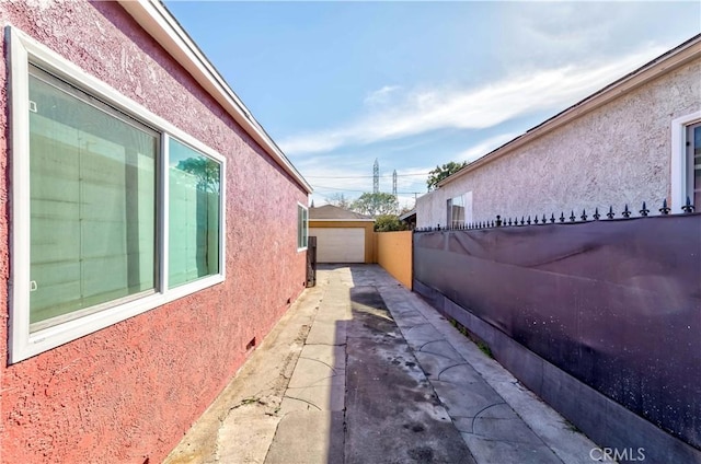 view of property exterior with a garage, an outdoor structure, fence, driveway, and stucco siding