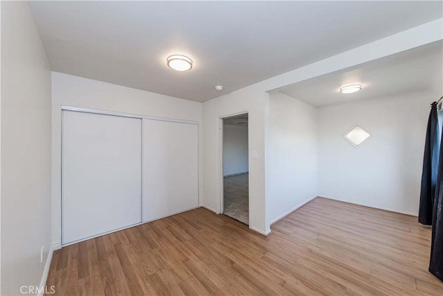 unfurnished bedroom featuring a closet, baseboards, and light wood finished floors