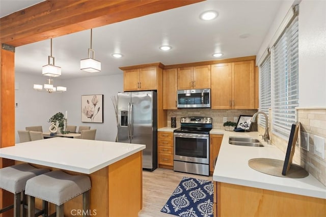 kitchen with a sink, a kitchen breakfast bar, light countertops, appliances with stainless steel finishes, and light wood finished floors