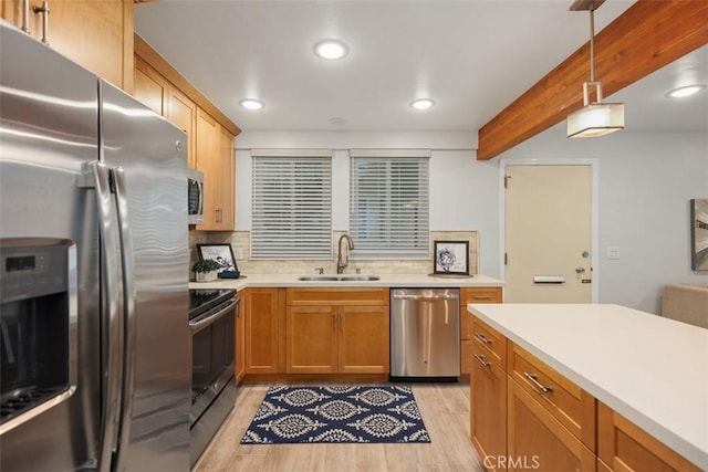 kitchen featuring pendant lighting, light wood finished floors, light countertops, appliances with stainless steel finishes, and a sink