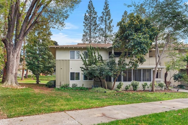 exterior space with a balcony, a front lawn, and stucco siding