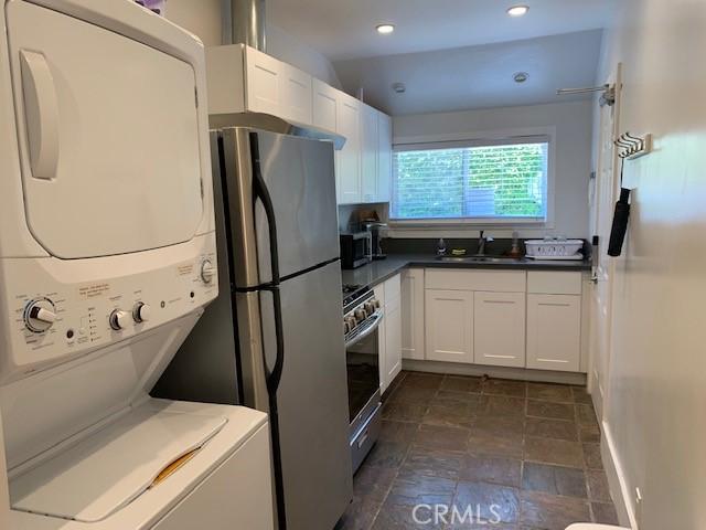 kitchen featuring stacked washer and dryer, a sink, white cabinets, appliances with stainless steel finishes, and stone finish floor