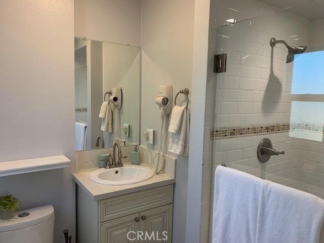 bathroom with toilet, tiled shower, and vanity