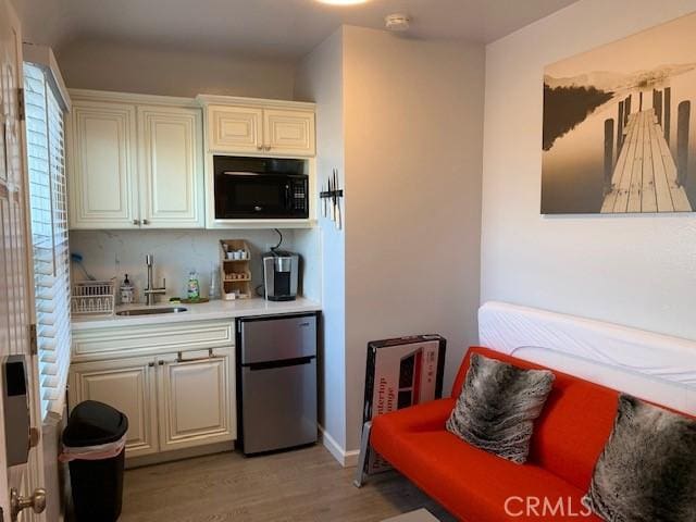 kitchen featuring black microwave, a sink, light countertops, fridge, and light wood finished floors