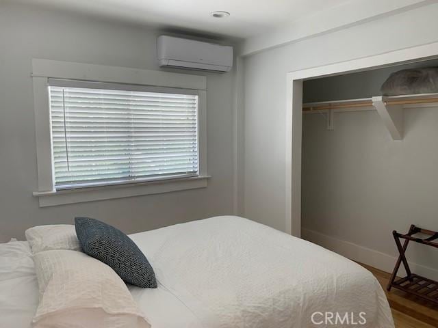 bedroom with wood finished floors, a wall mounted AC, a closet, and baseboards