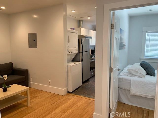 interior space with electric panel, white cabinetry, light wood-style flooring, and stacked washing maching and dryer