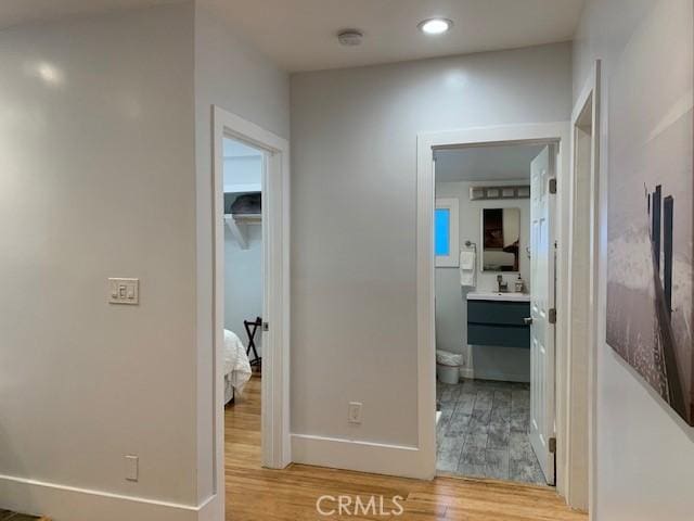 hall with a sink, recessed lighting, wood finished floors, and baseboards