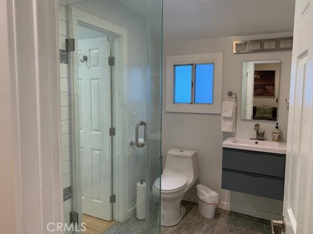 bathroom with wood finished floors, a shower stall, toilet, and vanity