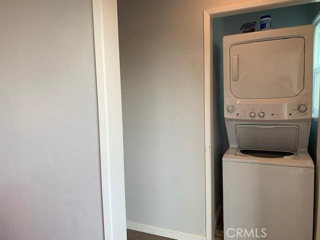 laundry area with laundry area, baseboards, and stacked washer / dryer