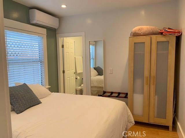 bedroom with recessed lighting, an AC wall unit, baseboards, and wood finished floors