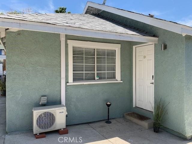 property entrance featuring a shingled roof, ac unit, and stucco siding