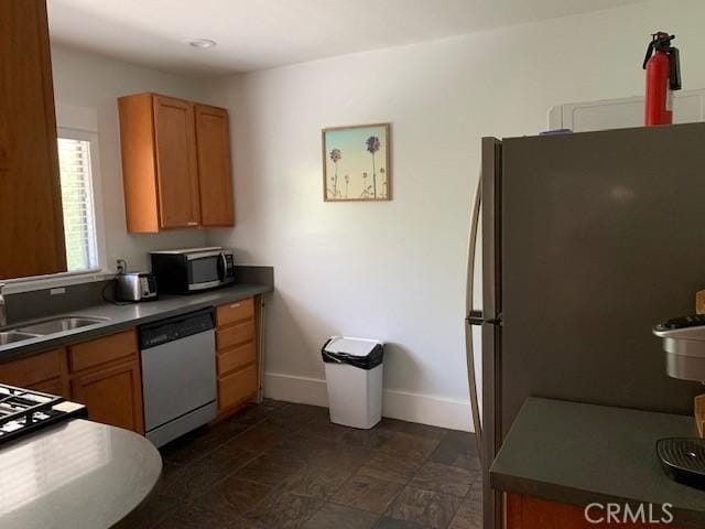 kitchen featuring dishwashing machine, stainless steel microwave, freestanding refrigerator, a sink, and baseboards