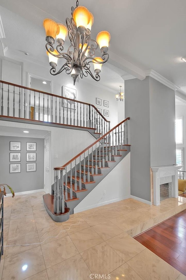 staircase featuring crown molding, a fireplace, a notable chandelier, and baseboards