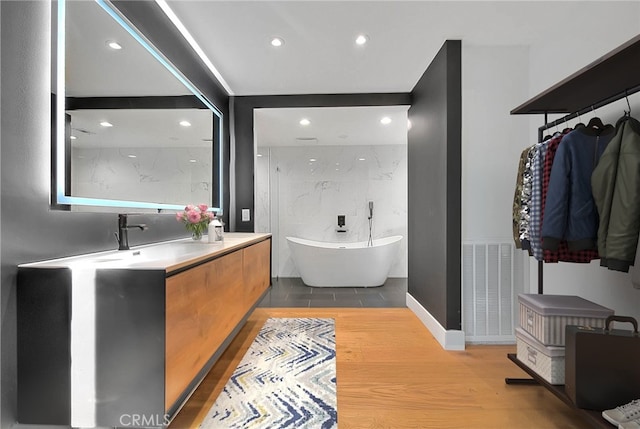 full bath with recessed lighting, wood finished floors, vanity, visible vents, and a soaking tub