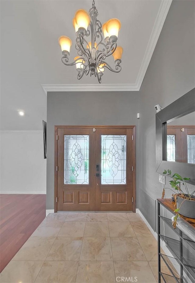 tiled entrance foyer featuring ornamental molding, a notable chandelier, and french doors