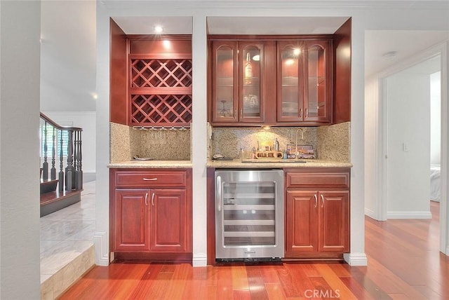 bar with a bar, wine cooler, light wood-type flooring, and decorative backsplash