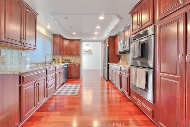 kitchen featuring stainless steel appliances, wood finished floors, ornamental molding, decorative backsplash, and a raised ceiling