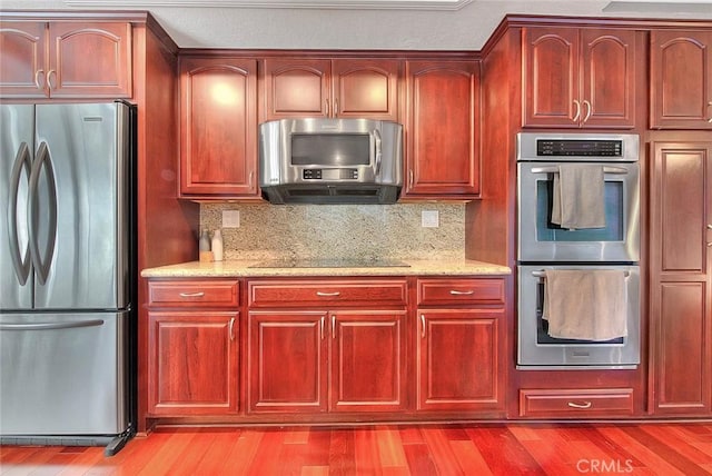 kitchen with reddish brown cabinets, light stone countertops, light wood-style flooring, and appliances with stainless steel finishes