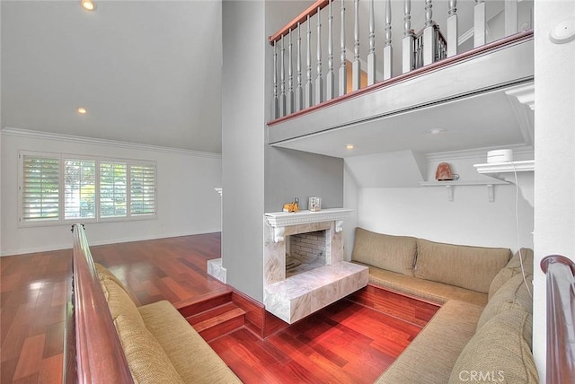 living area with a high ceiling, a premium fireplace, ornamental molding, wood finished floors, and baseboards