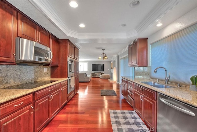 kitchen with reddish brown cabinets, a raised ceiling, appliances with stainless steel finishes, crown molding, and a sink