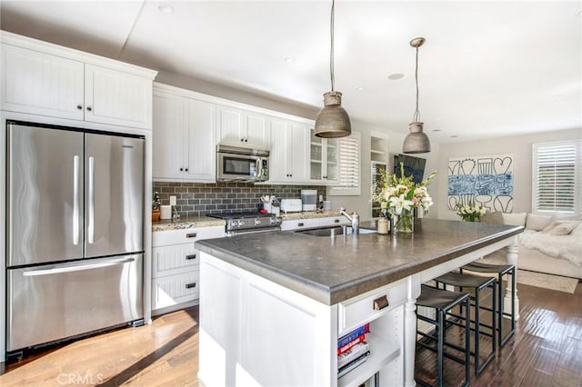 kitchen with stainless steel appliances, white cabinets, a kitchen island with sink, a sink, and a kitchen bar