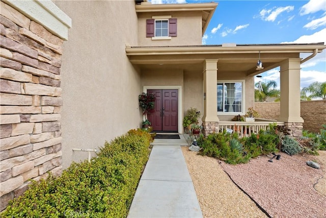 doorway to property with covered porch, stone siding, fence, and stucco siding