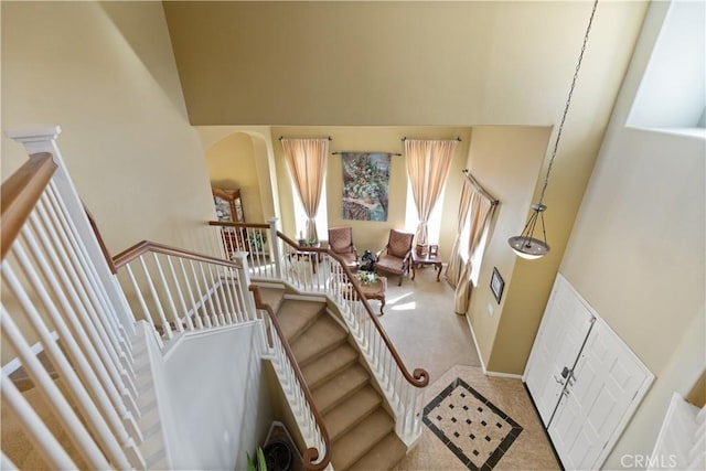 stairway featuring arched walkways, carpet floors, a high ceiling, and baseboards