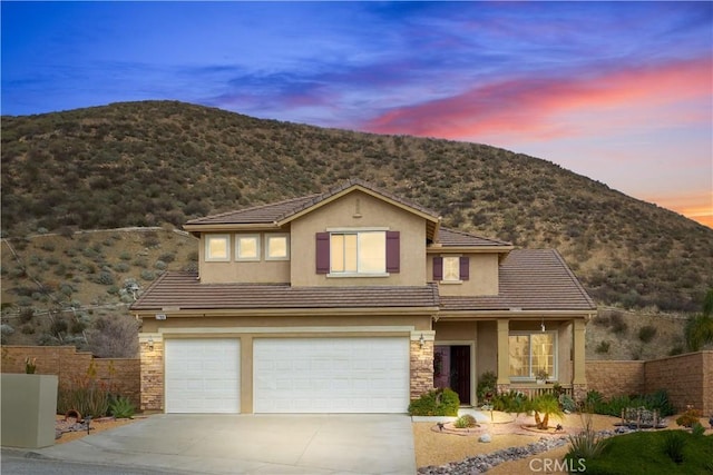 traditional-style home with stone siding, fence, driveway, and stucco siding