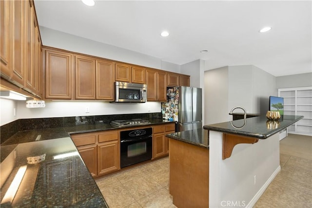 kitchen with appliances with stainless steel finishes, brown cabinetry, dark stone countertops, and recessed lighting