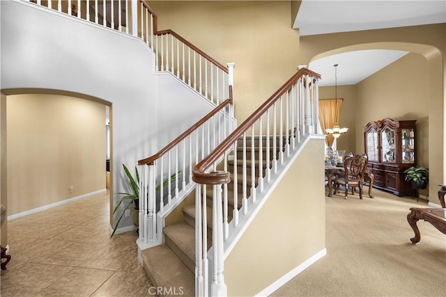 staircase featuring a high ceiling, baseboards, arched walkways, and a chandelier