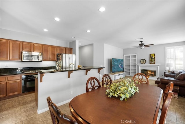 dining space featuring light tile patterned floors, built in features, a glass covered fireplace, ceiling fan, and recessed lighting