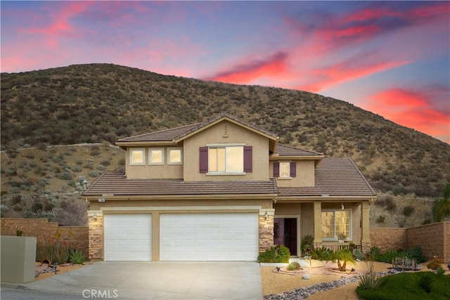 traditional home featuring stone siding, fence, driveway, and stucco siding