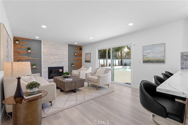 living area with recessed lighting, a large fireplace, light wood-style flooring, and baseboards