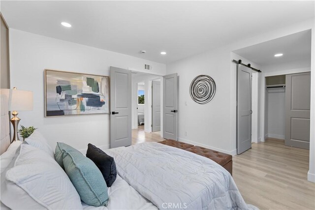 bedroom with recessed lighting, baseboards, light wood finished floors, and a barn door