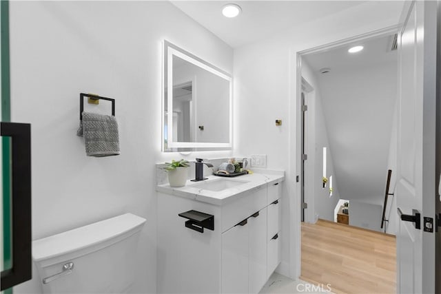 half bathroom featuring recessed lighting, vanity, toilet, and wood finished floors