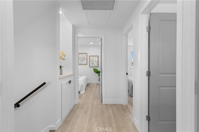 hallway featuring light wood-style floors, baseboards, visible vents, and an upstairs landing