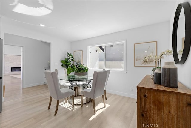 dining space featuring baseboards, a stone fireplace, and light wood-style floors