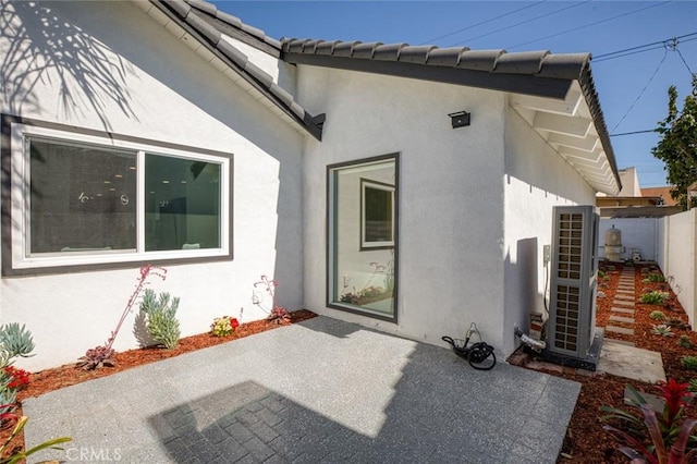 property entrance with a patio area, a tile roof, fence, and stucco siding