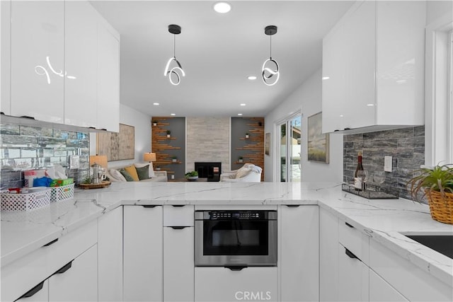 kitchen with oven, a peninsula, white cabinetry, light stone countertops, and decorative light fixtures