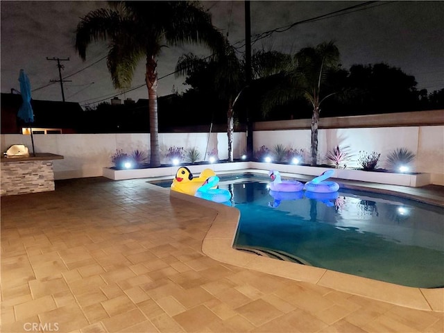 pool at night featuring a jacuzzi and a fenced in pool