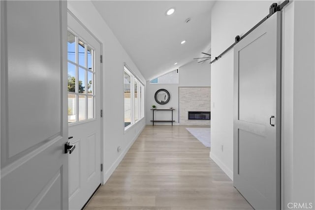 hallway with a barn door, recessed lighting, baseboards, vaulted ceiling, and light wood finished floors