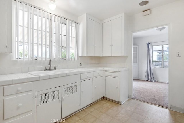 kitchen featuring tile counters, white cabinets, a wealth of natural light, and a sink