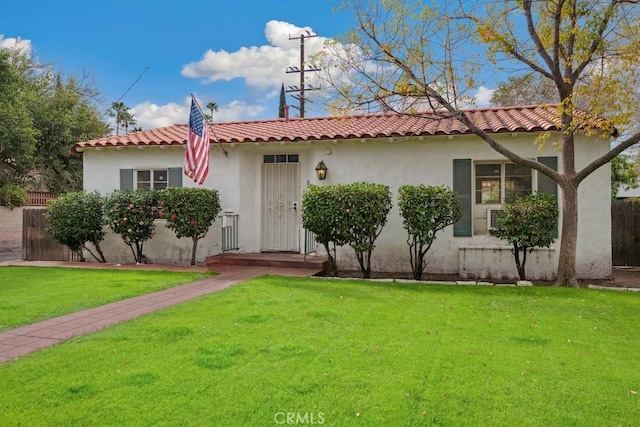 mediterranean / spanish-style house featuring a front yard, a tiled roof, fence, and stucco siding