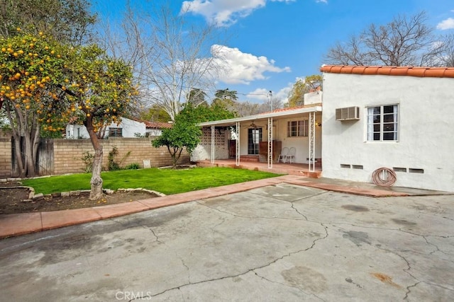 view of front facade featuring stucco siding, a front lawn, a tile roof, fence, and a patio area