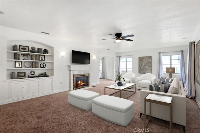 living area featuring visible vents, a brick fireplace, built in features, carpet floors, and a ceiling fan